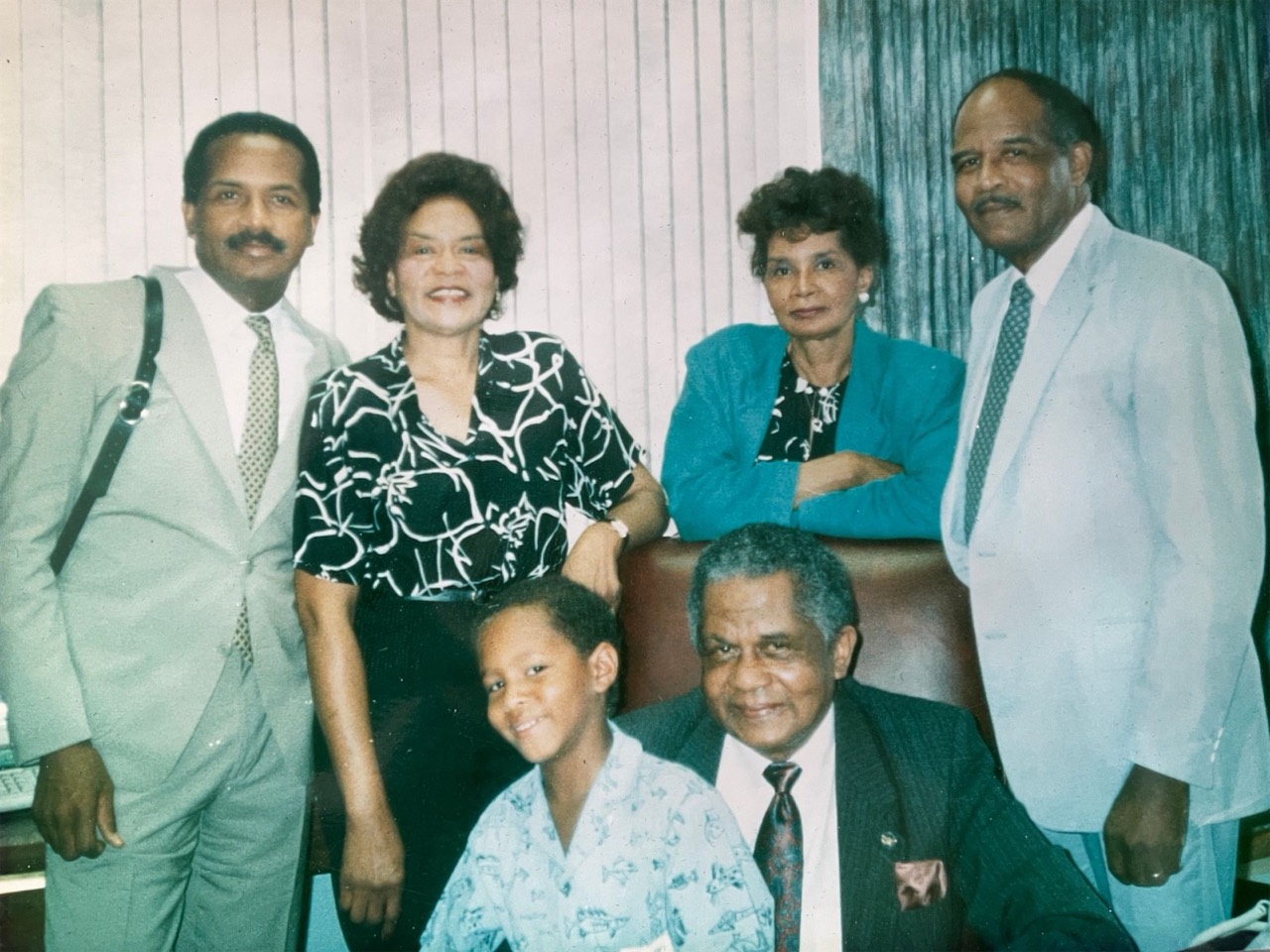 The Nero family elders in an office: four standing, David M. Nero Jr. seated, and a young boy at his side
